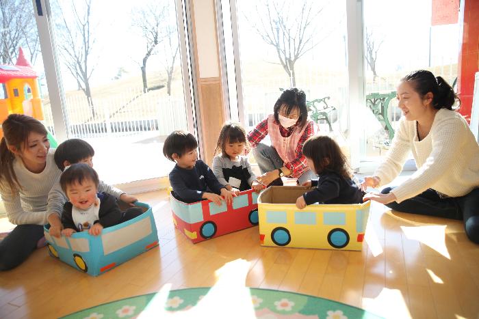 バスの入れ物に入る子どもを押すお母さんや先生達