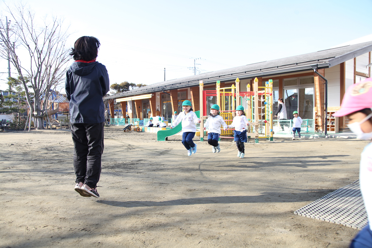 グラウンドで飛んでいる先生と園児の様子
