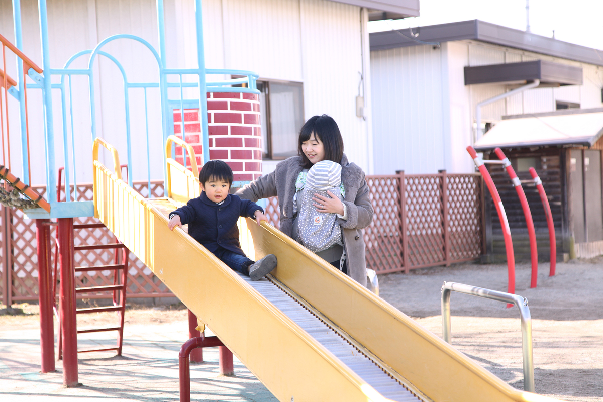 滑り台を滑る子どもを支えるお母さん
