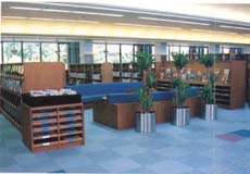 中央市立田富図書館の内観写真。ライトブルーを基調とした桝目の床に茶色の本棚が無数に並び、中央にはブルーのイスが写っています。