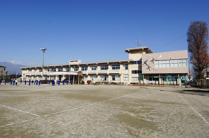 中央市立田富小学校の外観写真。前面に大きく広がるグラウンドの奥に、白い横長の校舎が写っています。
