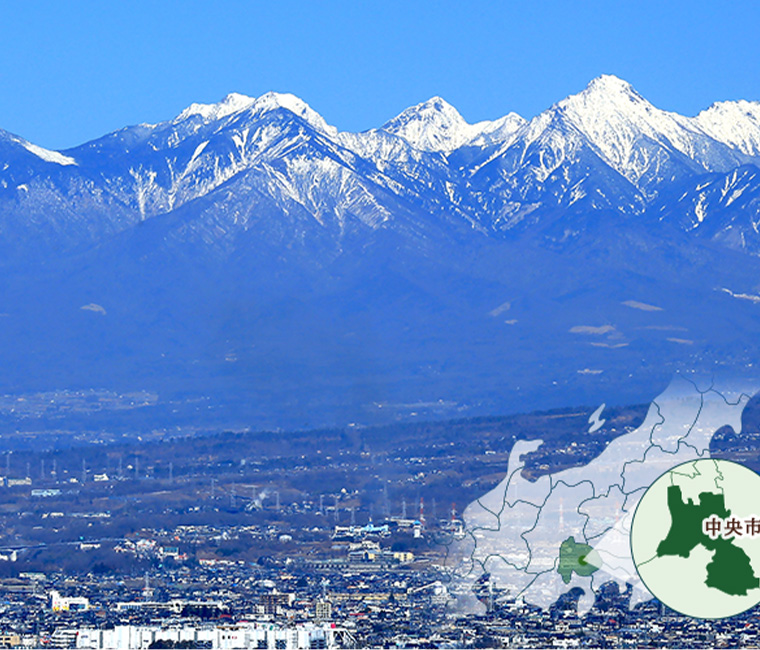 青空と雪を冠する八ヶ岳連峰のコントラストが美しい背景に中央市を眼下に望む風景。右下に山梨県の国中地方、甲府盆地の南部にある中央市の位置を指示した図。
