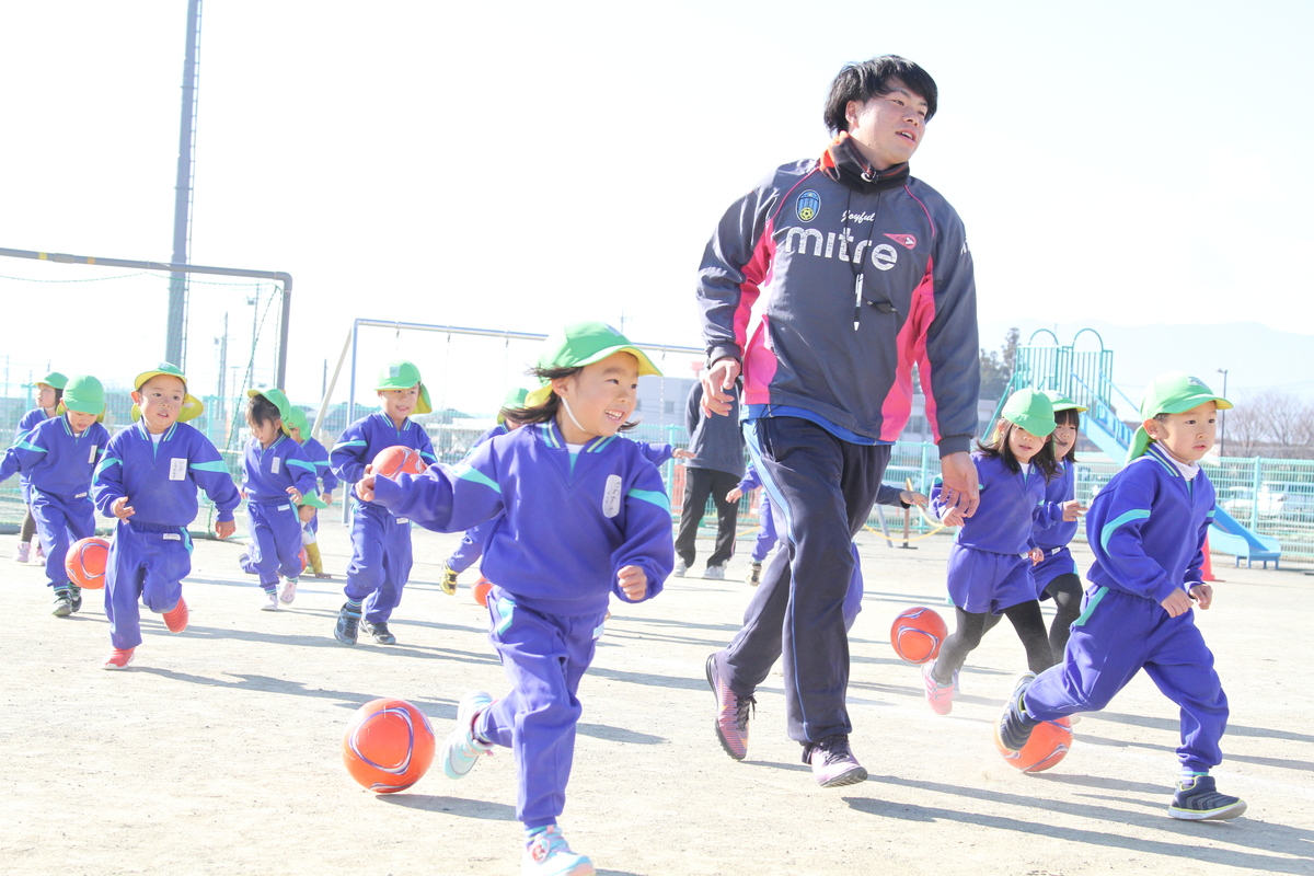 講師の先生と園児がグラウンドでサッカーをしている様子