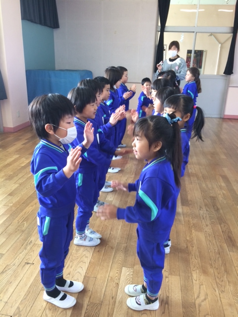 歌に合わせて向き合ったペアで互いの手をたたく子どもたち