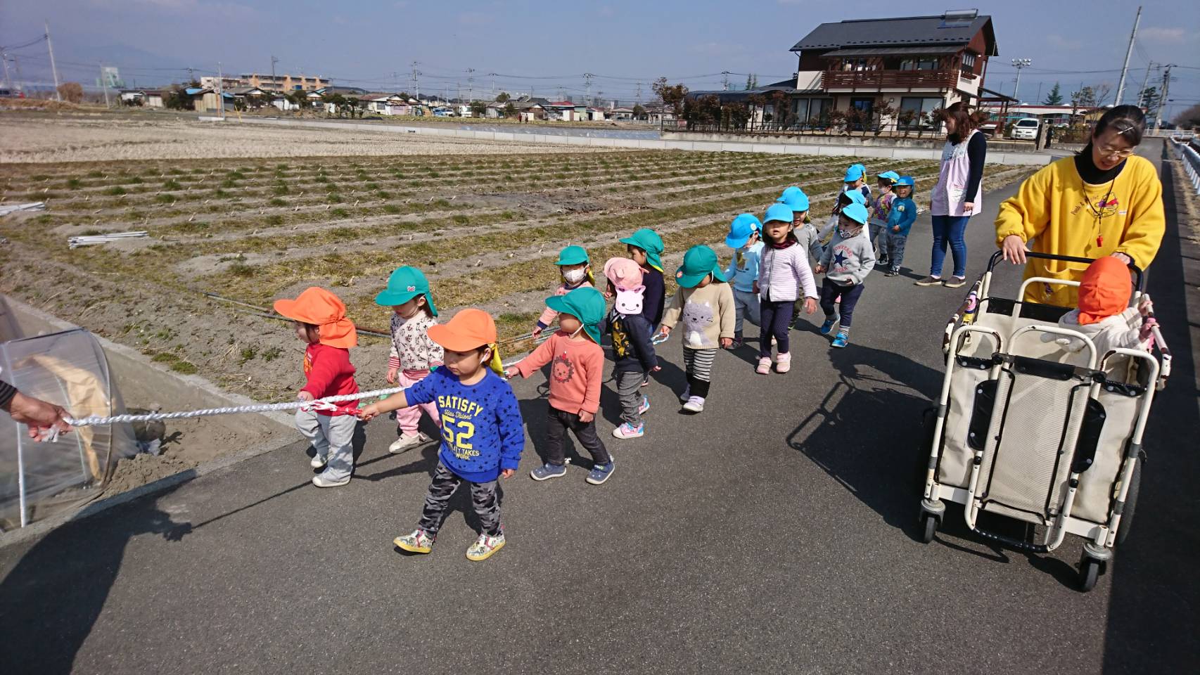 保育士が持つロープを持ちながら散歩する3歳未満児