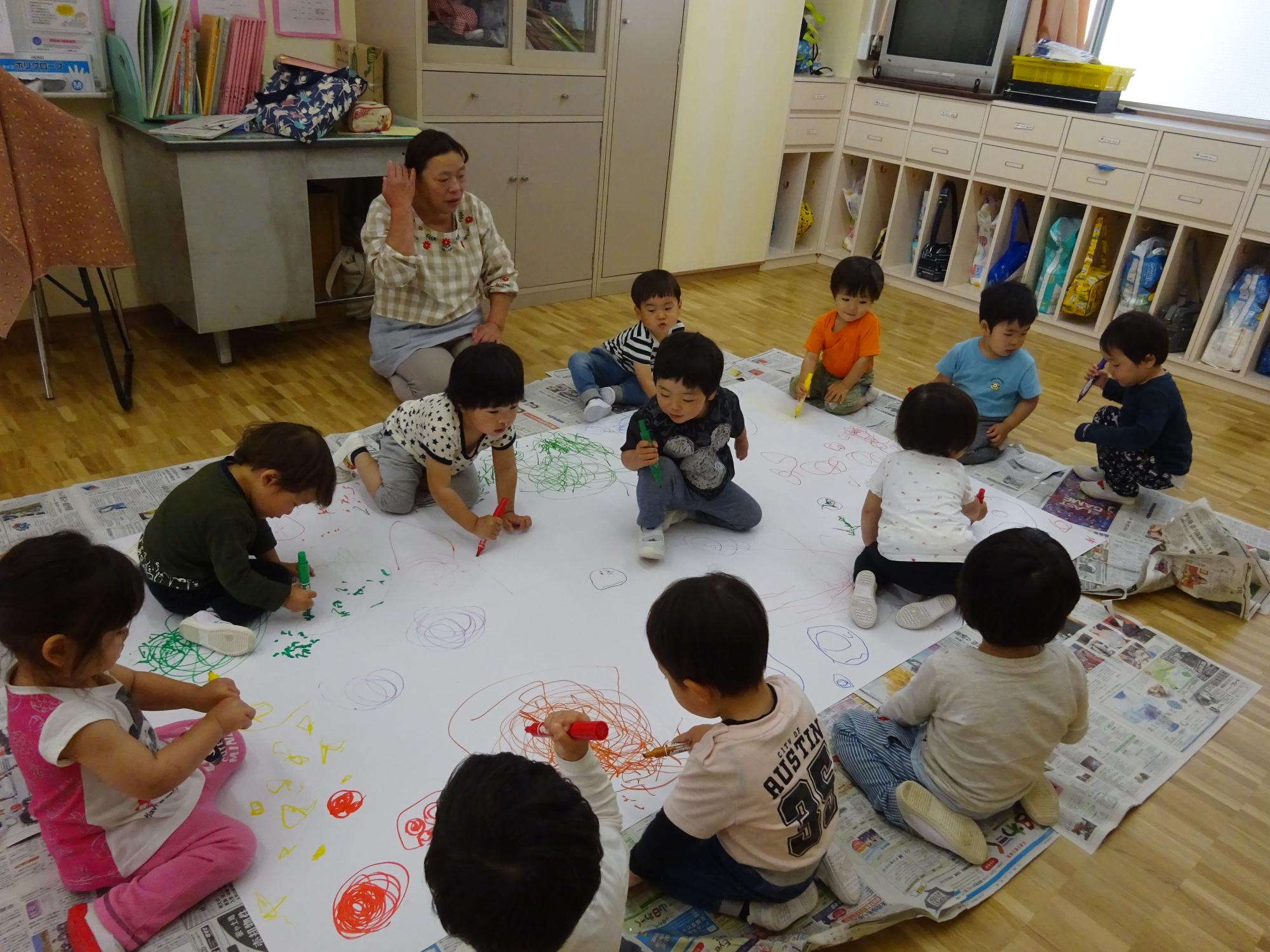 大きな紙にペンでお絵かきをする2歳児