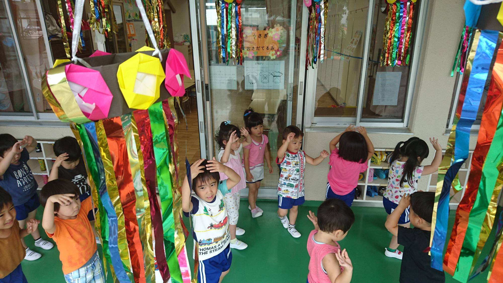 祭り飾りの下で盆踊りを踊る3歳児の子どもたち