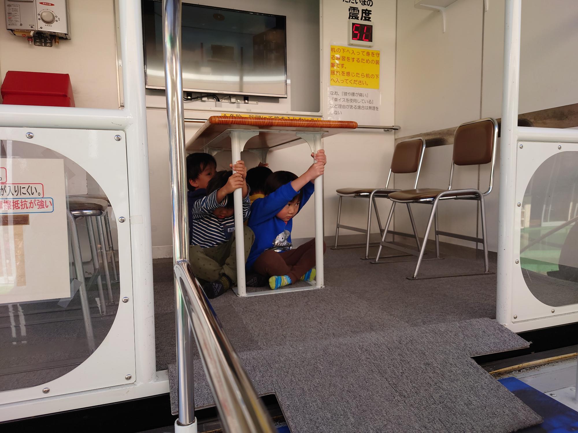 机の脚を持ち起震車を体験する4歳児の子どもたち
