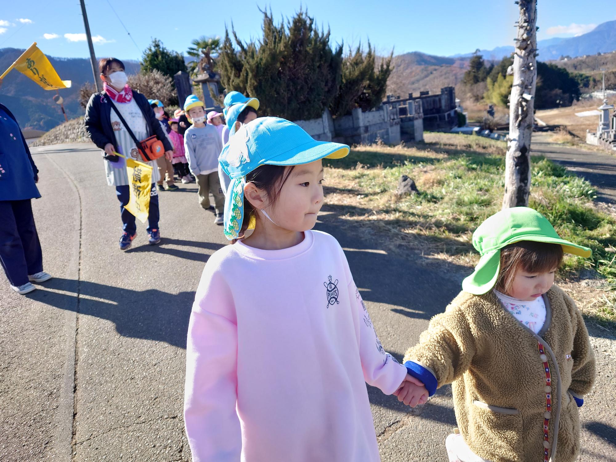 1歳児と手をつなぎ道路の端を歩く5歳児