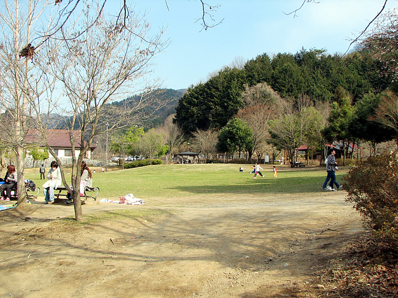 シルクの里公園における園内の風景写真。ベンチに座ってくつろぐ人や、散歩を楽しんでいる人々がいる。